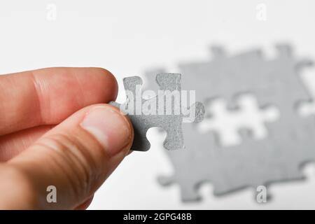 Photo of a person adding last piece of jigsaw puzzle to fit together on white background Stock Photo