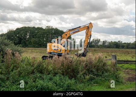 A  digger maintaining drainage ditches on low-lying grazing marsh on the Norfolk Broads at Buckenham Marshes Stock Photo