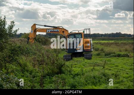 A  digger maintaining drainage ditches on low-lying grazing marsh on the Norfolk Broads at Buckenham Marshes Stock Photo