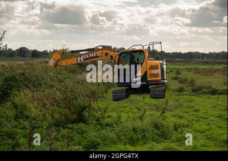 A  digger maintaining drainage ditches on low-lying grazing marsh on the Norfolk Broads at Buckenham Marshes Stock Photo