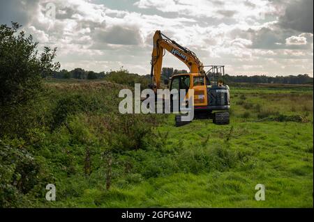 A  digger maintaining drainage ditches on low-lying grazing marsh on the Norfolk Broads at Buckenham Marshes Stock Photo