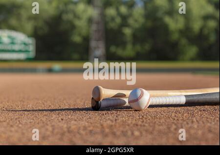 Low angle view of a baseball and wooden bats on dirt infield of baseball park in afternoon sunlight Stock Photo