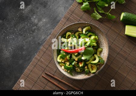 Asian spicy broken cucumbers salad with cilantro, ginger, pepper chili, black vinegar on black background. Copy space. Spicy cucumbers. Traditional co Stock Photo