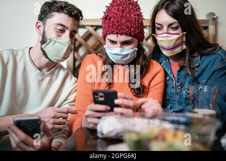 Best friends using mobile smartphone in coffee pub bar during corona virus outbreak - Food and technology concept Stock Photo