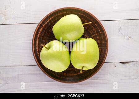 Three juicy green apples on a platter of clay on a wooden table, close-up, top view. Stock Photo