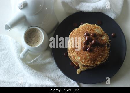 Stack of Oats Choco chips pancakes along with coffee for breakfast. Healthy pancakes made of oats flour loaded with chocolate chips. Shot on white bac Stock Photo