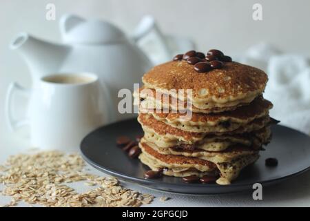 Stack of Oats Choco chips pancakes along with coffee for breakfast. Healthy pancakes made of oats flour loaded with chocolate chips. Shot on white bac Stock Photo