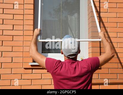 Contractor installing mosquito wire screen on house window to protect from insects. Mosquito wire screen installation. Stock Photo