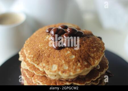 Stack of Oats Choco chips pancakes along with coffee for breakfast. Healthy pancakes made of oats flour loaded with chocolate chips. Shot on white bac Stock Photo