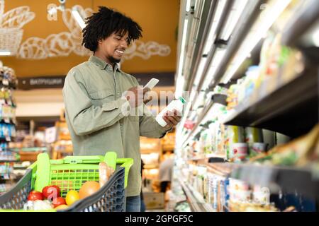 Black Guy Scanning Milk With Smartphone Buying Food In Supermarket Stock Photo