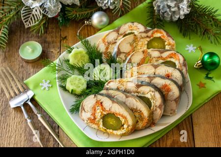 Festive snack. Baked mackerel roll stuffed with cheese, carrots, eggs and pickled cucumber, served on the Christmas table. Stock Photo
