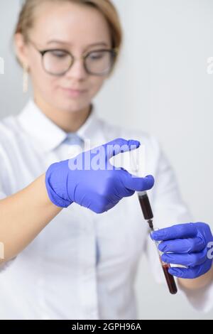 Doctor in latex gloves holding syringe with blood sample and test tube Stock Photo