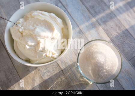 Step by step the process of making sour cream. Sour cream and sugar are prepared on a wooden table. Stock Photo