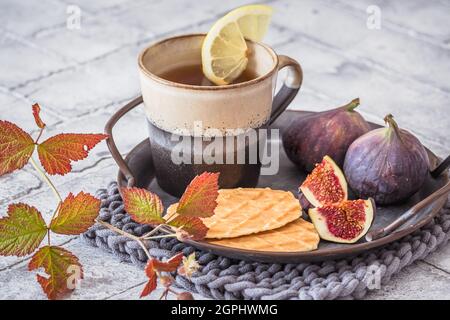 Cup of tea with cookies and fresh figs on a metal tray on gray tiles Stock Photo