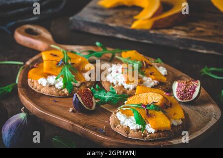 Round crispbread slices with grainy cream cheese, roasted pumpkin and rocket salad on wooden background Stock Photo