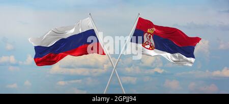 flags of Russia and Serbia waving in the wind on flagpoles against sky with clouds on sunny day. Symbolizing relationship, dialog between two countrie Stock Photo