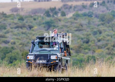 Safari tourists stand to train their long telephoto lenses on wildlife from a typical open jeep safari vehicle in Masai Mara, Kenya