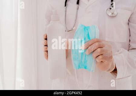 Doctor shows a disinfectant gel and a face mask for covid-19 virus Stock Photo