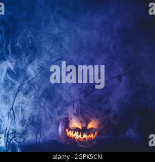Spooky Halloween jack o lantern pumpkin with carved scary face glowing and billowing smoke in the night. Stock Photo