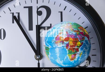 black clock with black digits and white dial behind a small colorful globe shows five to twelve Stock Photo