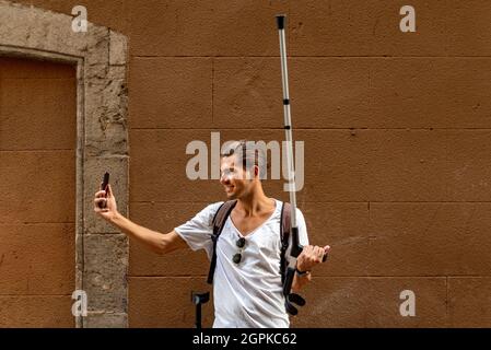 Young man with crutches taking a selfie with his mobile in the street Stock Photo