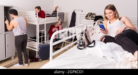 Woman lying on bed in hostel with smartphone Stock Photo