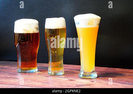 Three different glass goblets with wheat, light and dark beer are on a wooden table. Close-up. Stock Photo