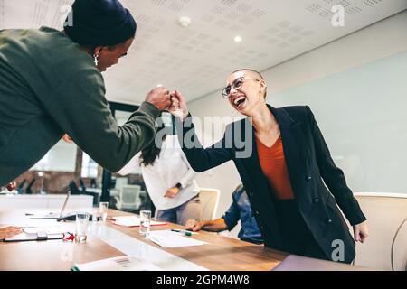 Young businesspeople fist bumping each other before a meeting in a boardroom. Two colleagues smiling cheerfully while greeting each other. Group of bu Stock Photo