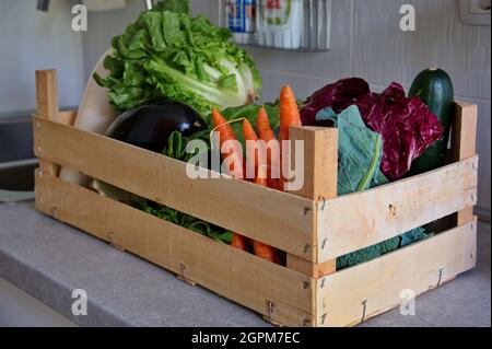 Healthy vegetables in wooden container on kitchen desk Stock Photo