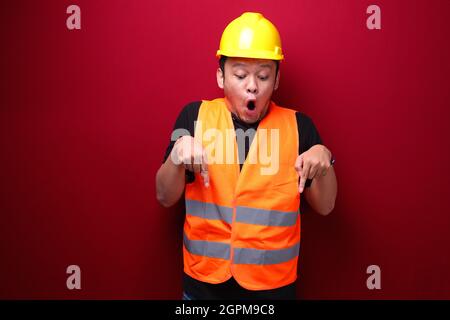 Wow Young asian man worker is surprised and shouting with pointing bottom with his hand on red background. Stock Photo