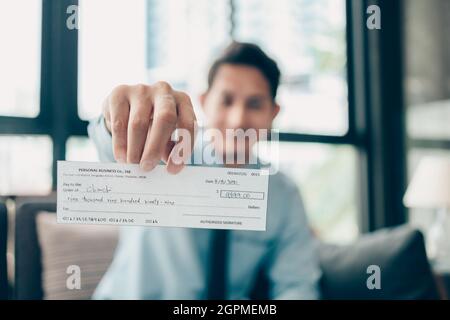 A Businessperson's hand giving cheque to customer and dollar bill, coin, laptop and graph chart on the desk at office. Payment by check, paycheck, pay Stock Photo