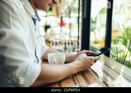young businessman working and using smart phone and notebook computer in workplace. Young freelance working in coffee shop. Stock Photo