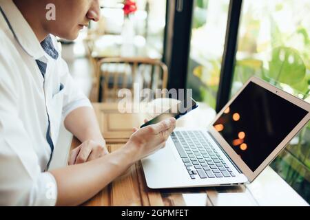 young businessman working and using smart phone and notebook computer in workplace. Young freelance working in coffee shop. Stock Photo