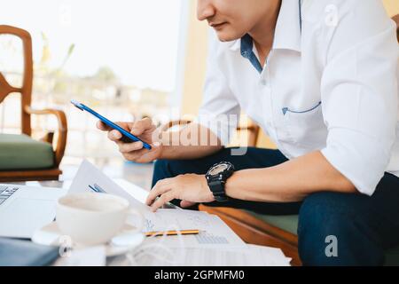 young businessman working and using smart phone and notebook computer in workplace. Young freelance working in coffee shop. Stock Photo