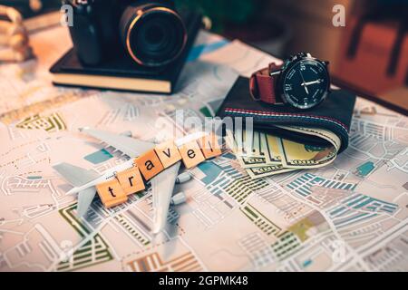 Wood square with word "travel", watch, money wallet, passport, airplane model, camera on road map. Object for travel concept. Stock Photo