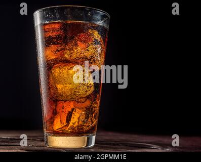 Chilled glass of cola drink with ice cubes isolated on dark background. Stock Photo