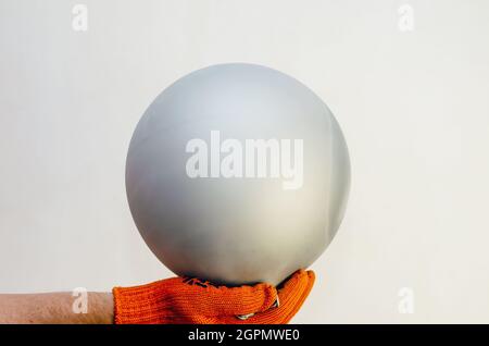 A hand in a red protective glove holds a gray balloon against th Stock Photo