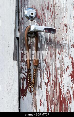 An old door detail. The paint is badly chipped, there is part missing from the door frame and an abandoned dog-collar is hanging from the handle. Stock Photo