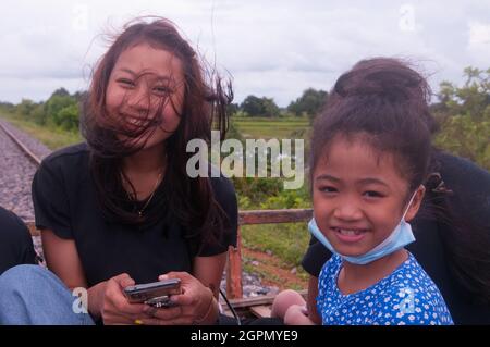 A beautiful mixed race woman (1/2 Burmese, 1/4 Laotian & 1/4 Cambodian) & a 9 year old Cambodian girl ride the Bamboo Train during the COVID - 19 pandemic & The Pchum Ben Buddhist holiday. Battambang Province, Cambodia. Sept. 24th, 2021. © Kraig Lieb Stock Photo