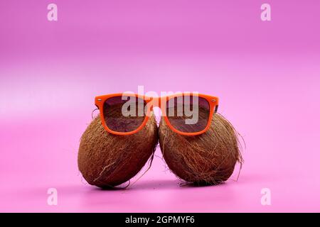 Two whole coconuts and orange glasses on a pink background.. Stock Photo
