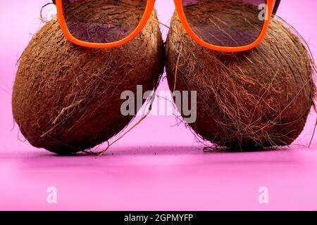 Two whole coconuts and orange glasses on a pink background.. Stock Photo