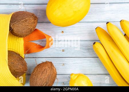 Whole coconuts in a yellow bag, bananas and melon on a blue wooden background. Stock Photo
