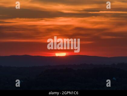 Sunset in the hilly countryside with big red sun and dramatic clouds Stock Photo