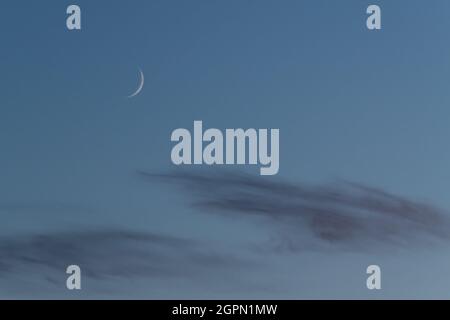 Waxing crescent moon phase of earth's natural satellite on blue sky above clouds Stock Photo