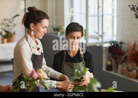 Waist up portrait of two female florists arraigning flower compositions in workshop and smiling Stock Photo