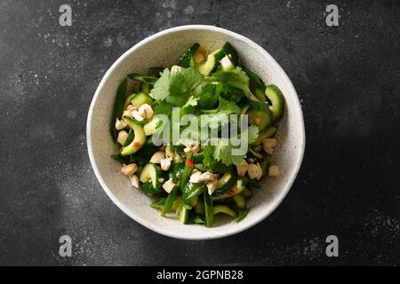 Asian Broken Cucumber salad with fresh coriander, ginger, chili pepper, black vinegar in white bowl isolated on black background. Spicy cucumbers. Pop Stock Photo