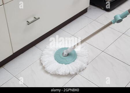 Blue cleaning mop on white ceramic tile floor in the kitchen Stock Photo