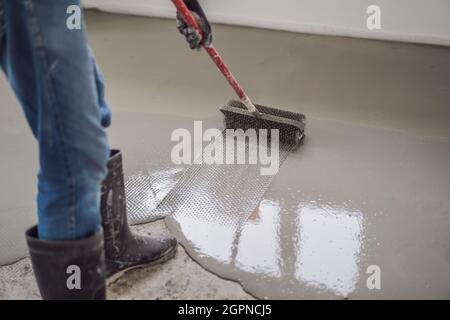 plasterer during floor covering works with self-levelling cement mortar, uses a needle roller Stock Photo