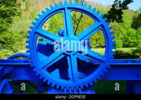 Large blue painted metal gear as a drive part for a water dam in a forest river Stock Photo