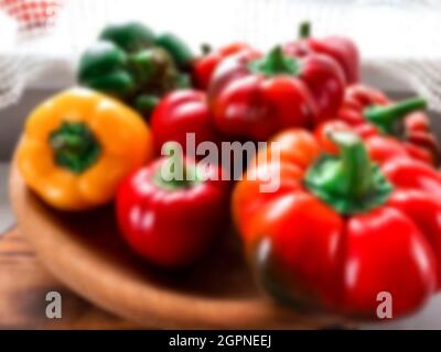 Blurred. Fresh harvest. Multi-colored textured peppers lie on a wooden plate against the background of the window. Colorful sweet bell peppers, natura Stock Photo